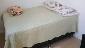 A small bed with a green textured bedspread, a floral pillow, and a matching pillow on a wooden floor. - O melhor de Madureira  (Rio de Janeiro)