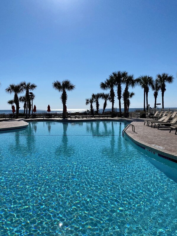 A clear blue pool with palm trees and lounge chairs, surrounded by a clear sky. - 3BR Oceanfront Escape w/ Panoramic Views! (Myrtle Beach)