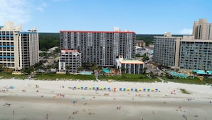 Un hotel frente a la playa con varios edificios altos, una piscina y una playa de arena con sombrillas.
