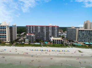 A beachfront hotel with multiple high-rise buildings, a swimming pool, and a sandy beach with umbrellas. - 3BR Oceanfront Escape w/ Panoramic Views! (Myrtle Beach)