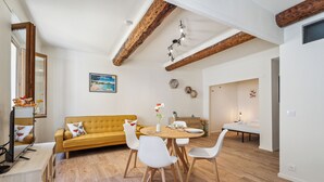 Un salon moderne avec un canapé jaune, des chaises blanches, une table à manger en bois et des poutres apparentes en bois au plafond.
