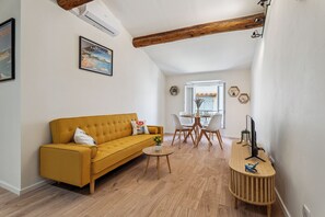 Ein modernes Wohnzimmer mit einem senffarbenen Sofa, einem kleinen runden Tisch und einem Holznachttisch mit einem Fernseher.