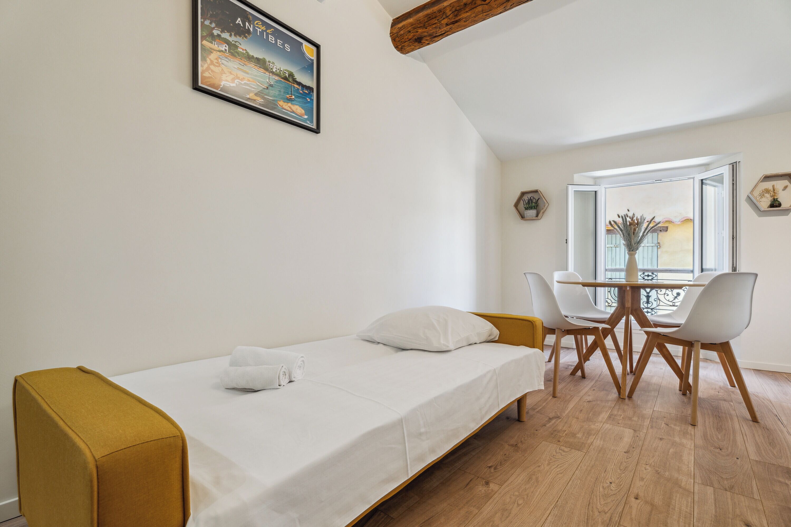 Une pièce comprenant un lit, une table avec des chaises, une fenêtre et un tableau accroché au mur.