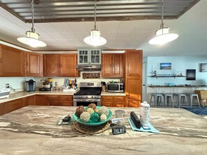 A kitchen with wooden cabinets, a central island, a stove, a microwave, and hanging pendant lights.