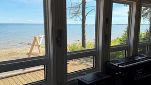 Een kamer met grote ramen met uitzicht op een strand, een bed met een beddeken met patroon en een toetsenbord op een bureau.