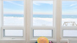 Een kamer met drie grote ramen met uitzicht op een besneeuwd strand.