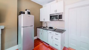 Una cucina compatta con mobili bianchi, un forno a microonde integrato e un frigorifero.