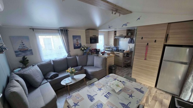 Ein kompakter Wohnbereich mit Sofa, Esstisch, Küchenzeile und einem kleinen Fenster.