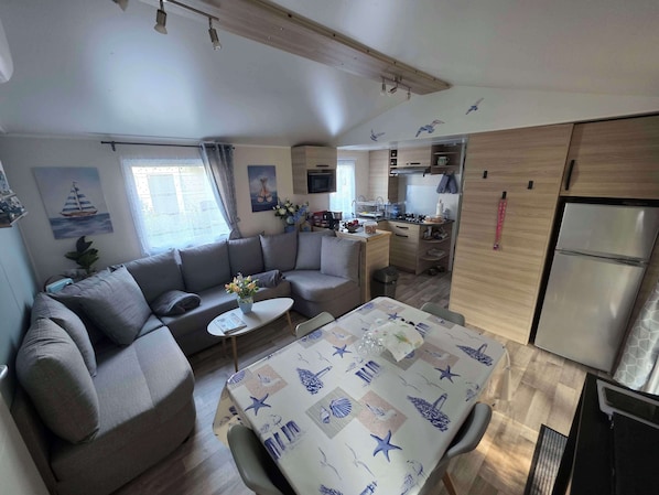 Ein kompakter Wohnbereich mit Sofa, Esstisch, Küchenzeile und einem kleinen Fenster.