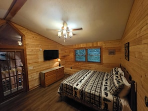 Ein Schlafzimmer in einer Blockhütte mit Bett, Schminktisch, Fernseher und Fenstern.