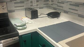 A kitchen with a toaster, a waffle maker, a stove, and a green cabinet.
