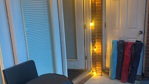 Un espacio de estar al aire libre techado con suelo a cuadros, una silla cubierta y una puerta con bolsos colgados.