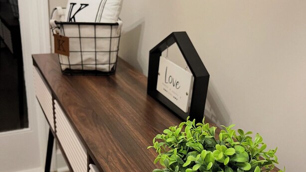Un banco de madera con una jardinera con plantas verdes, un cojín blanco con un diseño negro y un cuadro con la palabra 'LOVE'.