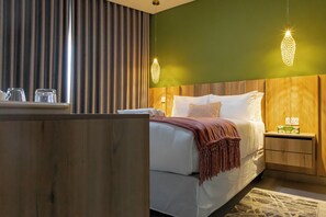 A hotel room with a bed, bedside table, and a nightstand with a lamp.