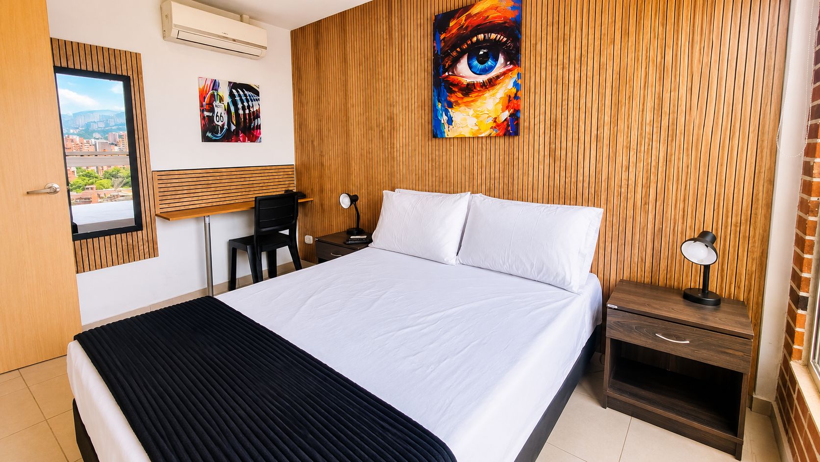 Ein Hotelzimmer mit Bett, Schreibtisch, Stuhl, Nachttisch und Bildern an den Wänden.