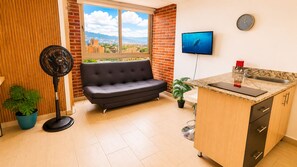Ein modernes Wohnzimmer mit einer Couch, einem Fernseher, einem Ventilator und einer Küchenzeile mit Spüle und Arbeitsfläche.