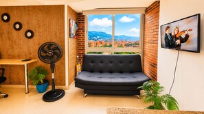 Un salon moderne avec un canapé noir, un mur en bois orné de motifs circulaires, un ventilateur, un téléviseur et une vue sur la ville.