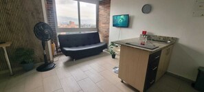 Ein modernes Wohnzimmer mit Sofa, Fernseher, einer kleinen Küchenzeile und Blick auf die Stadt.