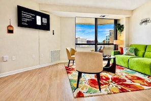 A modern living room with a green sofa, a beige armchair, a small table, and a large window with a city view. - New! AMZN HQ-Luxe DCA-Captivating View- DC Airport (Arlington)