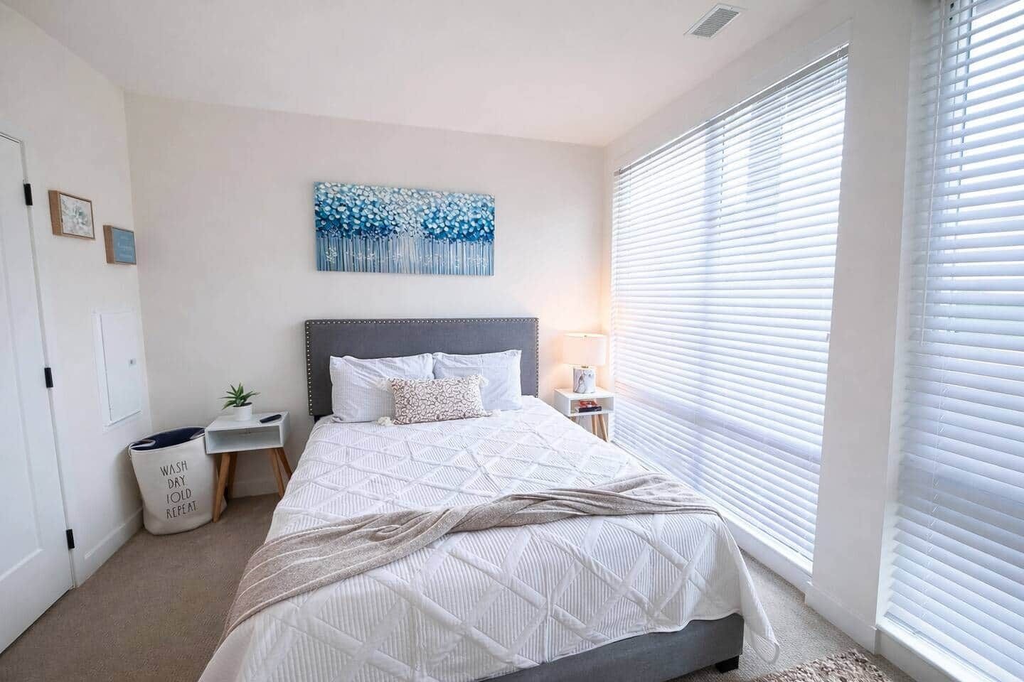 A bedroom with a bed, a nightstand, a wall art piece, and a window with blinds.