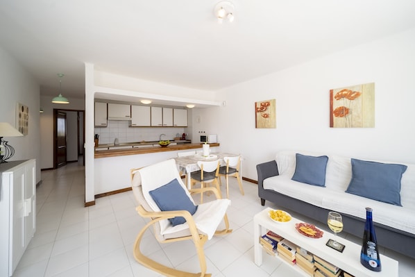 A modern living room with a sofa, a rocking chair, and a dining area with a table and chairs. - Apto 115 (Costa Teguise)