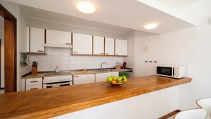 Una cucina moderna con mobili bianchi, un piano di lavoro in legno, un forno a microonde e una ciotola di frutta.