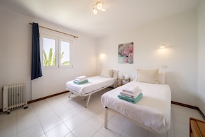 A hotel room with two beds, a window with curtains, a radiator, and a wall-mounted picture. - Apto 115 (Costa Teguise)
