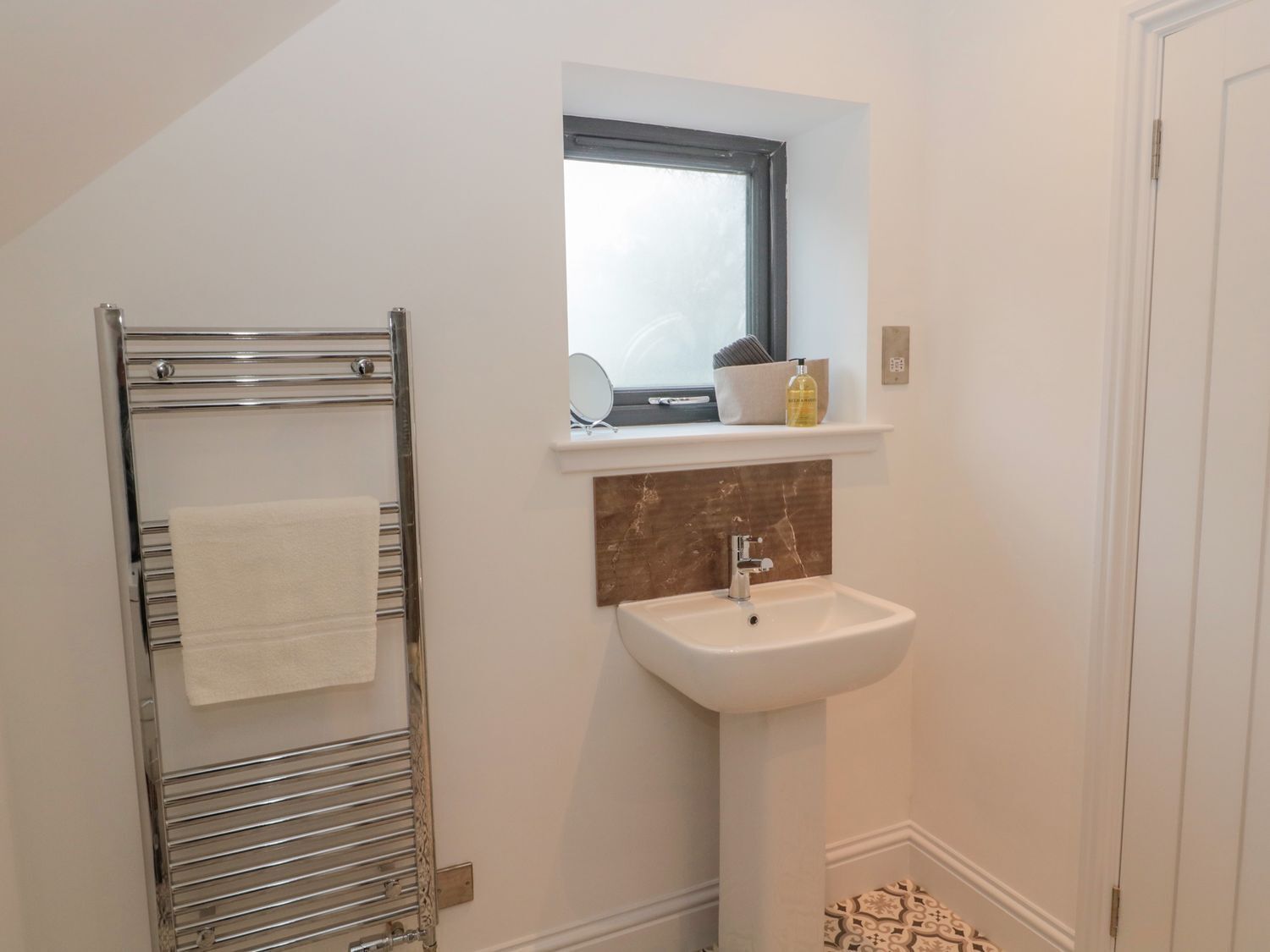 A bathroom with a towel rack, a sink, a mirror, and a window.