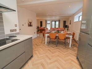 A modern kitchen with a built-in stove, dining area with a wooden herringbone floor, and a large refrigerator. - Harvest Cottage 1 (Berwick-upon-Tweed)