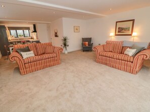 A living room with two striped sofas, a potted plant, a fireplace, and a kitchen in the background. - Harvest Cottage 1 (Berwick-upon-Tweed)