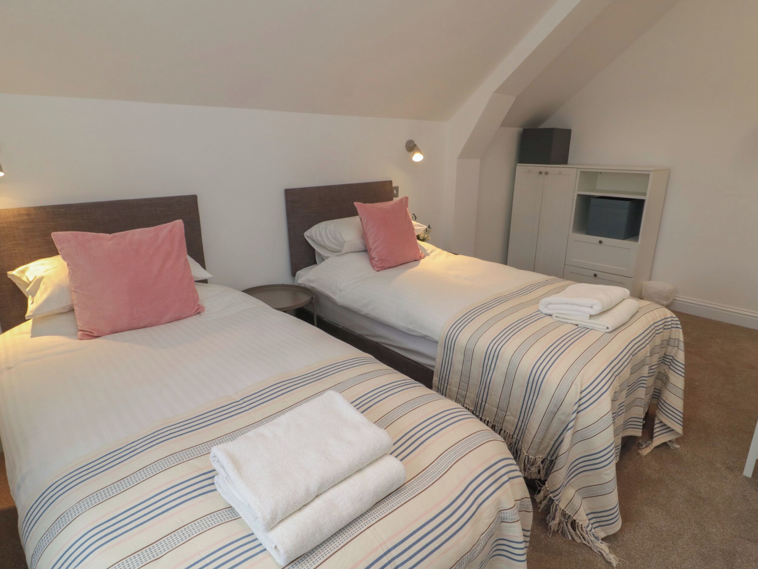 A bedroom with two beds, each with a pillow and a folded towel. There is a TV on a cabinet and a small round table between the beds.