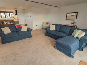 A living room with two blue sofas, a dining table, and a kitchen area. - Harvest Cottage 2 (Berwick-upon-Tweed)
