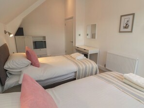 A bedroom with two beds, a desk, a mirror, and a radiator. - Harvest Cottage 2 (Berwick-upon-Tweed)