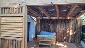 Una terraza de madera con un jacuzzi, un banco y una pérgola.
