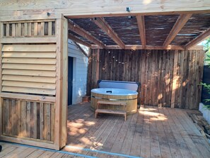 A wooden deck with a hot tub, a bench, and a pergola structure.