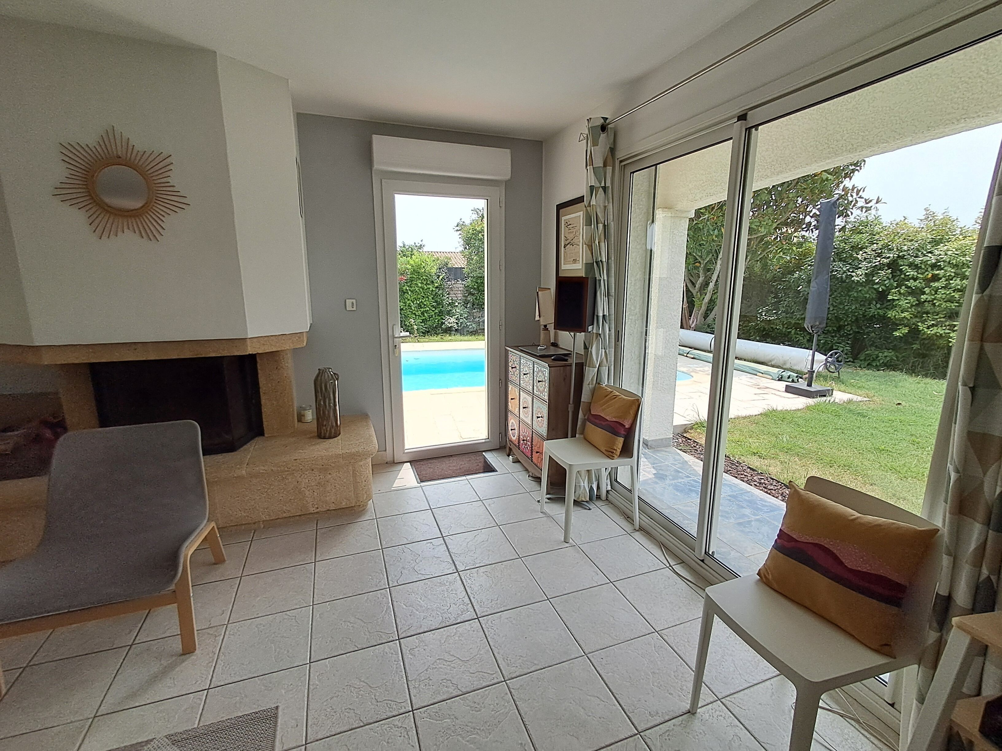 En stue med pejs, sofa, spisebord og udsigt til swimmingpool og have.