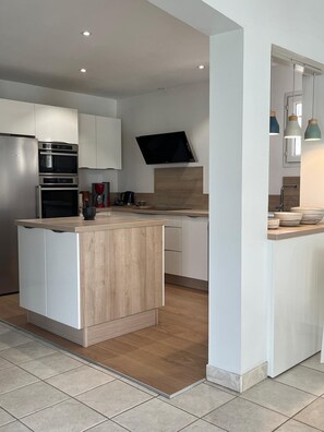 A modern kitchen with built-in appliances, a wooden island, and pendant lighting.