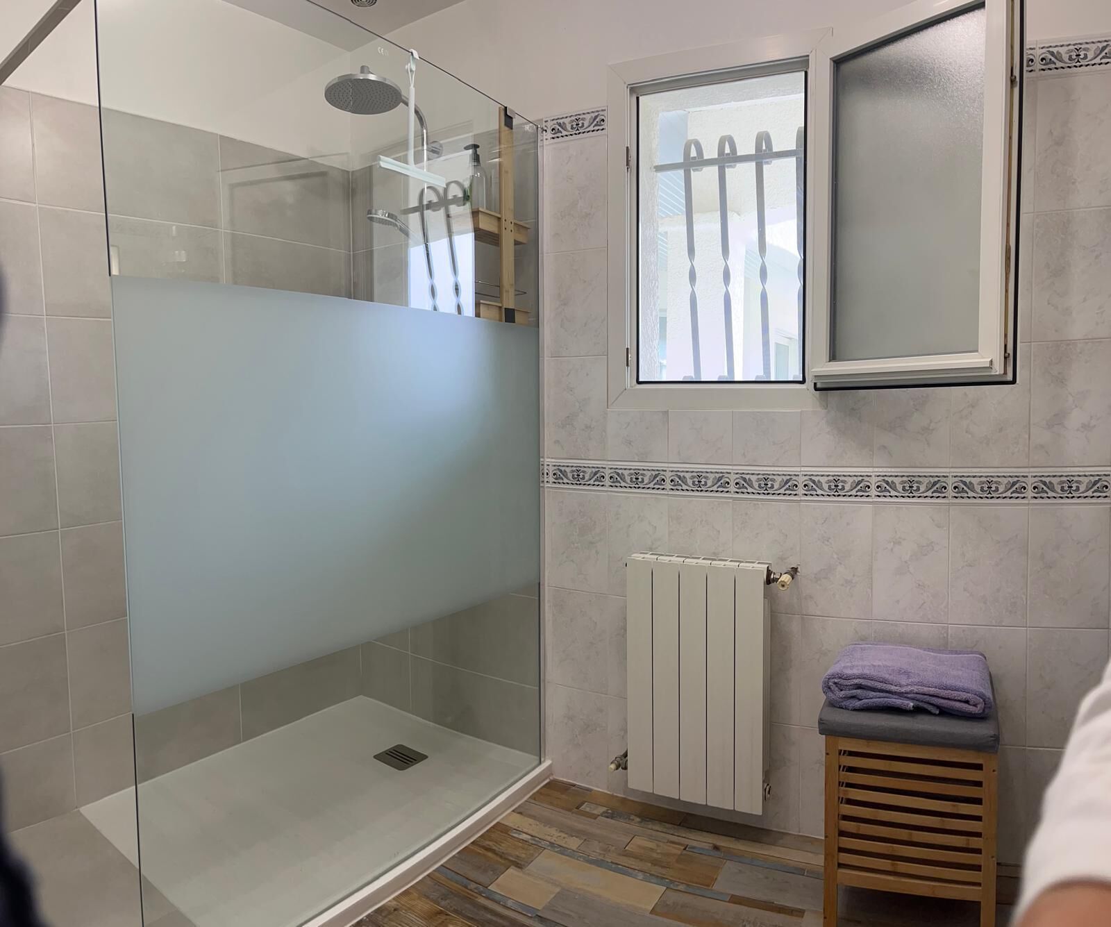 Une salle de bain avec une douche à parois de verre, une fenêtre et un radiateur.