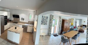 A modern kitchen with a built-in dishwasher, a dining area with a wooden table and chairs, and a living room with a sofa and a fireplace.