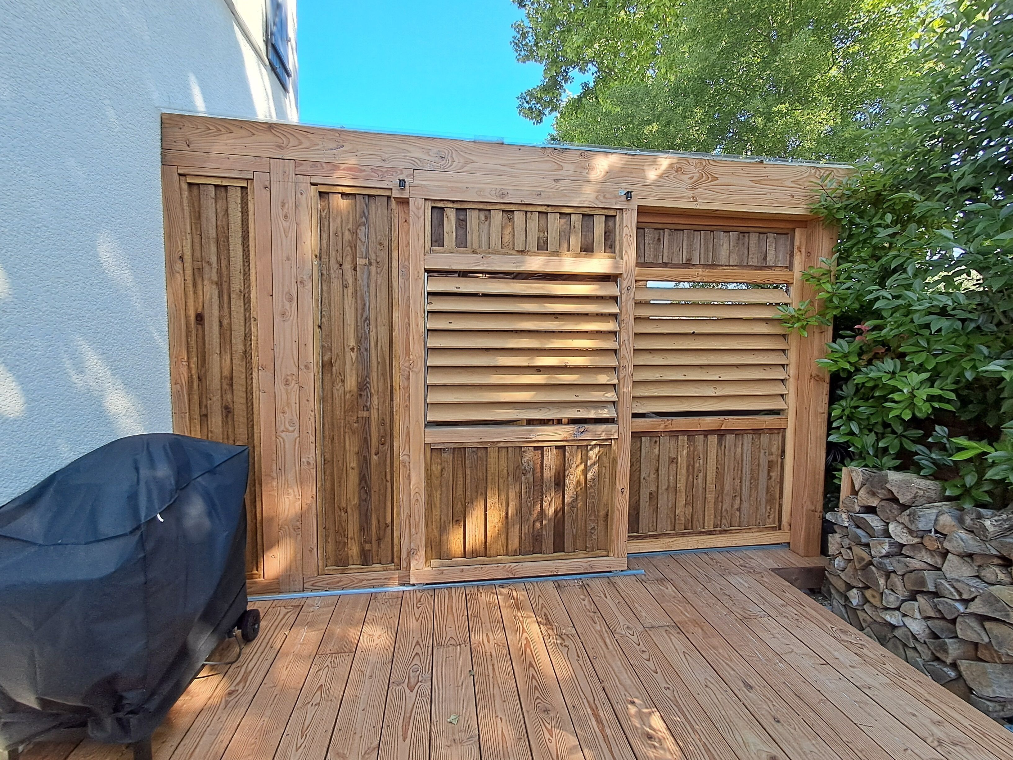 Une terrasse en bois avec un barbecue et un mur en pierre.