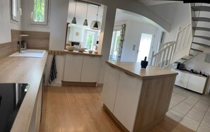 A modern kitchen with wooden cabinetry, a central island, and a staircase leading to an upper level.