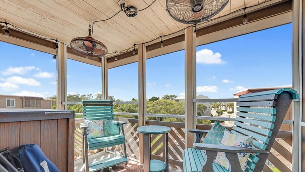 Un espacio exterior techado con sillas y una mesa, ventanas amplias y vistas del paisaje circundante.