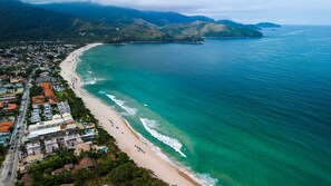 Vista aérea de uma cidade costeira com praia, casas e uma cordilheira ao fundo.