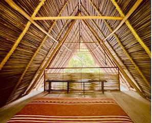 An attic room with a sloped roof, a bench, and a view of greenery outside.