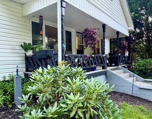 A porch with a bench, potted plants, and a hanging flower arrangement.