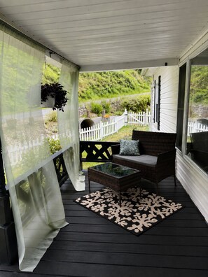 A covered porch with a wicker sofa, a glass coffee table, and a patterned rug.