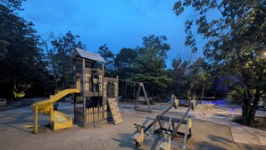 Un parque infantil con tobogán, muro de escalar y columpios.