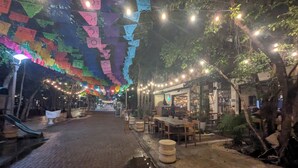Un área de comedor al aire libre con suelo de ladrillo, mesas, sillas y luces colgantes.