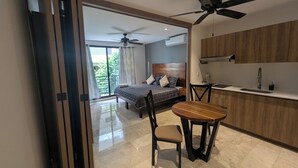 Una habitación de hotel moderna con cama, mesa de comedor, sillas, ventilador de techo y una zona de cocina.