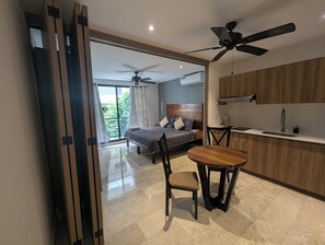 Ein modernes Hotelzimmer mit Bett, Esstisch, Stühlen, Deckenventilator und Küchenzeile.